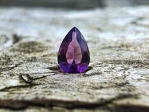 A pear-cut purple gemstone stands, with its point upwards, on the ground.